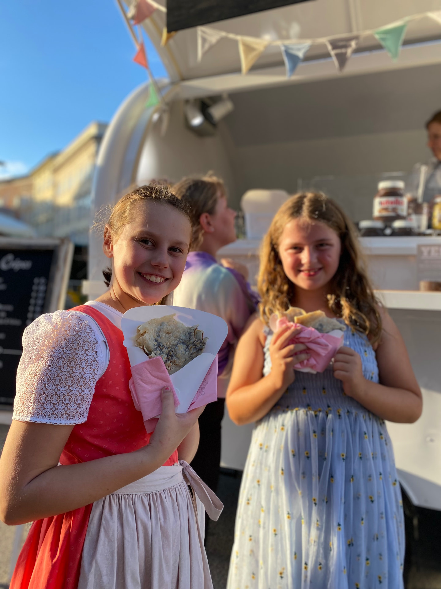 Zwei Mädchen mit frisch gebackenen Crêpes am Crêpe-Trailer beim Rupertikirtag in Salzburg